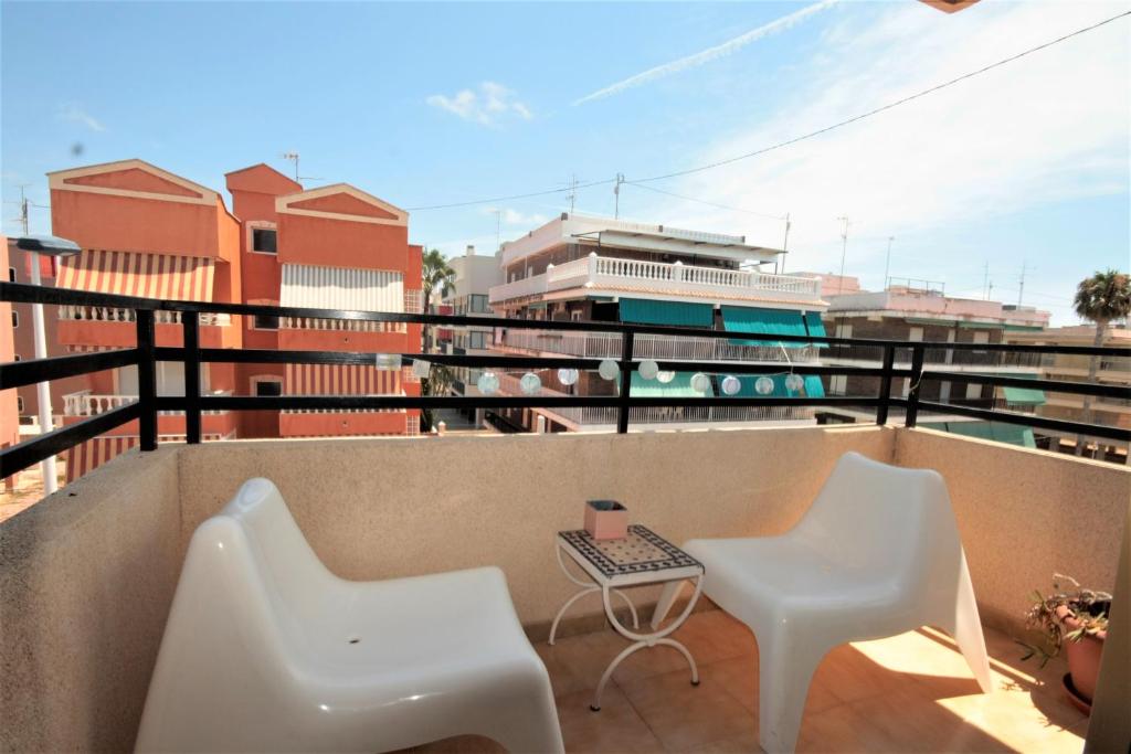 Un balcón con 2 sillas blancas y una mesa. en Estudio Gran Playa, en Santa Pola