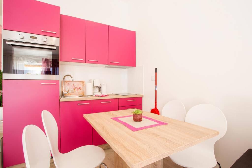 een keuken met roze kasten en een houten tafel en stoelen bij Apartman Cone in Pula