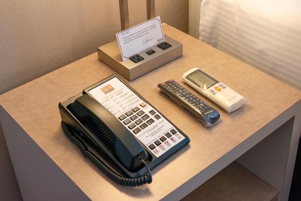 A bedside tabletop with a telephone, television remotes and power outlets.