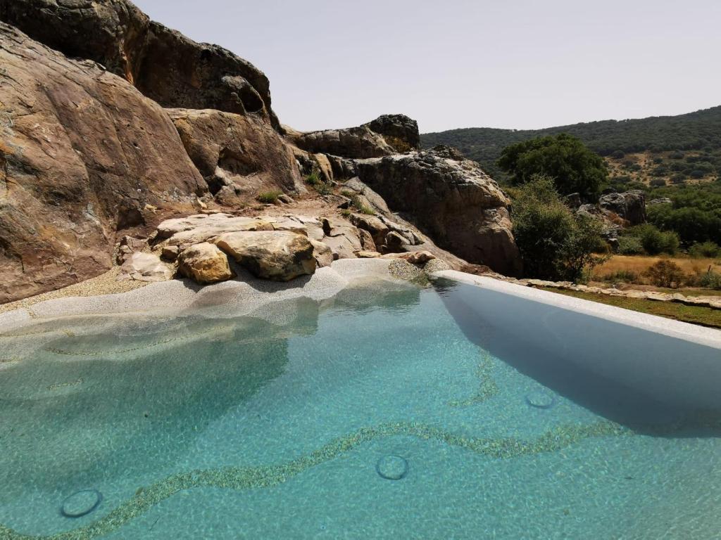 a swimming pool with blue water and rocks at Tambor Del Llano in Grazalema