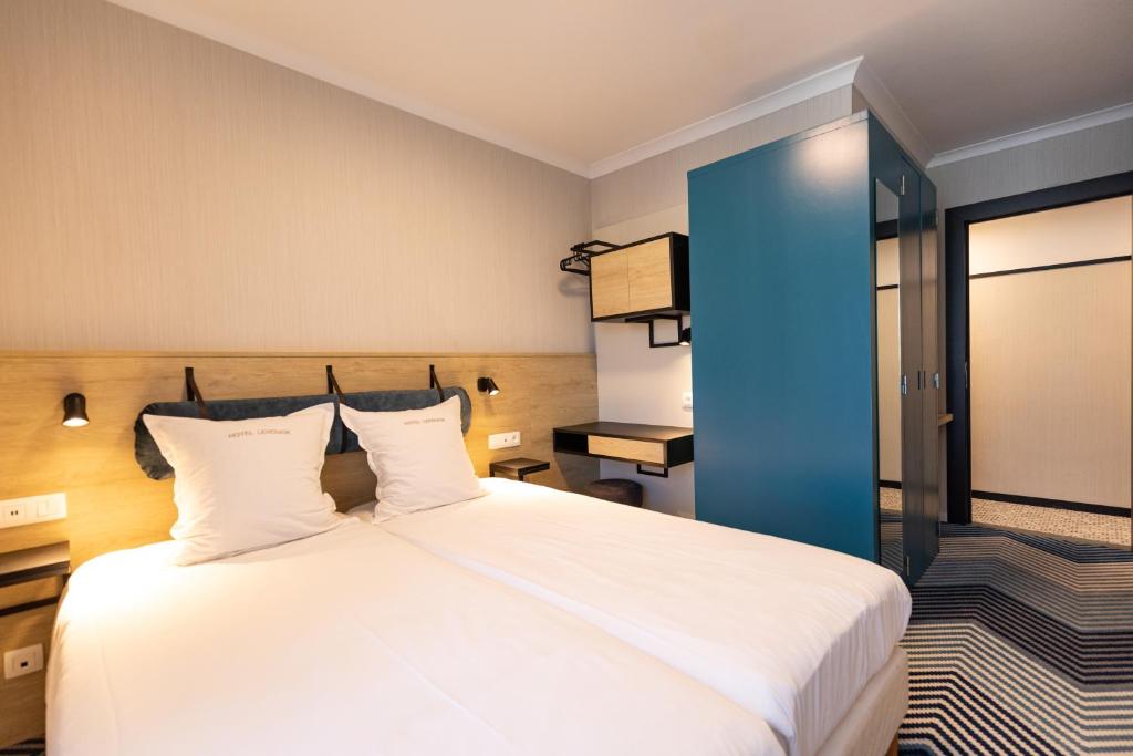 a bedroom with a large white bed with a blue door at HOTEL LEHOUCK in Koksijde