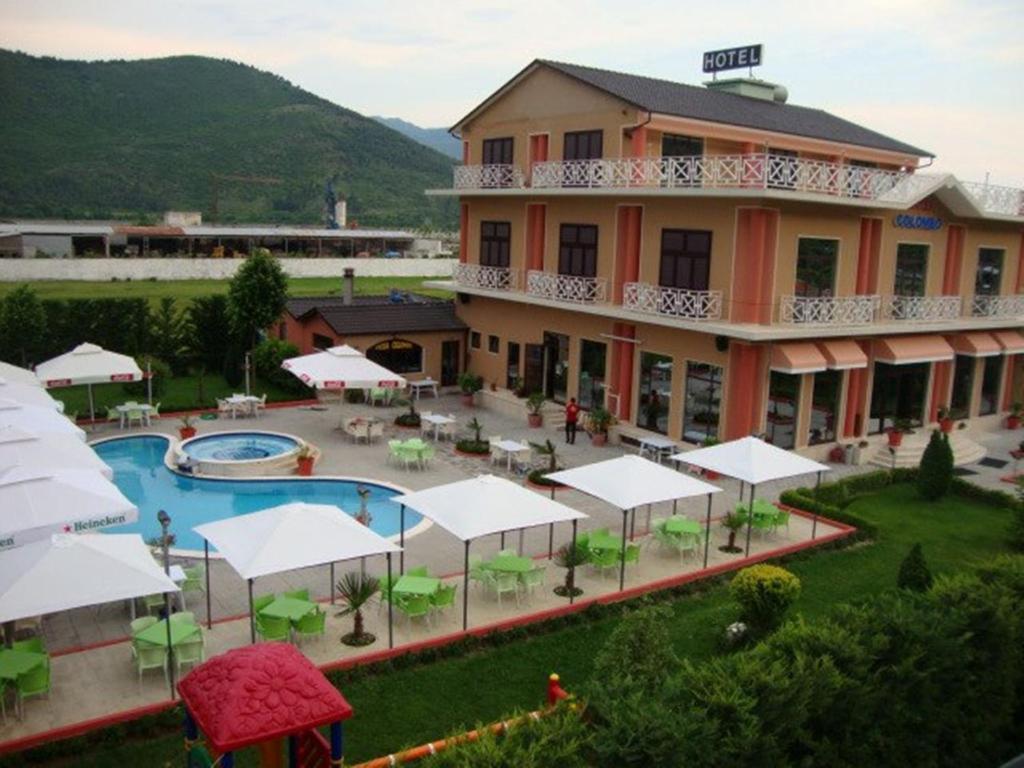 a large building with a pool and tables and white umbrellas at Hotel Colombo in Elbasan