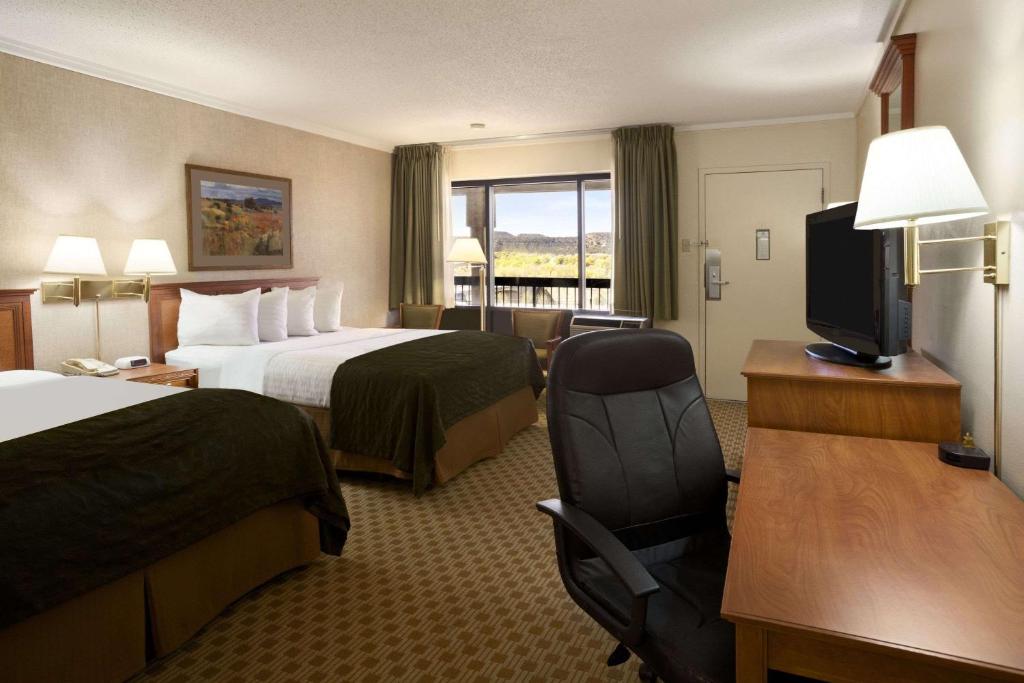 a hotel room with two beds and a desk and a television at Days Inn & Suites by Wyndham Trinidad in Trinidad
