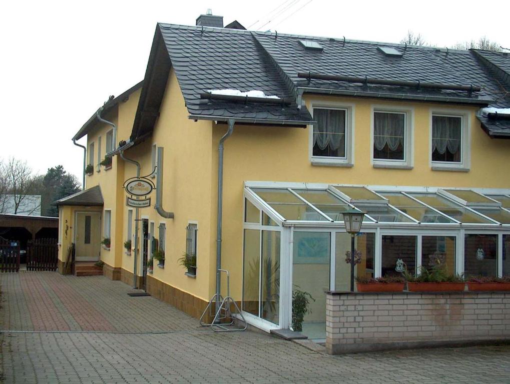 ein gelbes Haus mit einem Gewächshaus an der Seite in der Unterkunft Gockescher Hahn in Pöhl