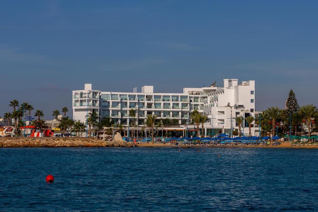 a large white building on a beach next to the water at Limanaki Beach Hotel & Suites in Ayia Napa