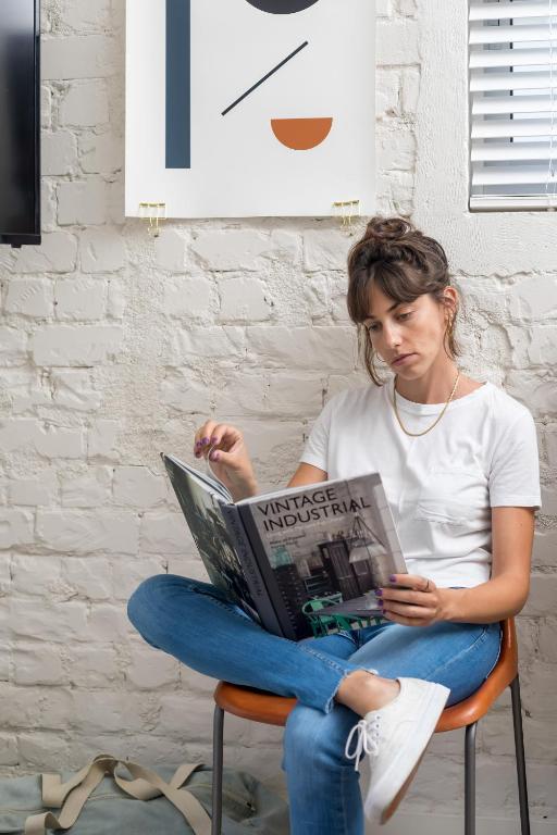 a woman sitting on a chair reading a magazine at The Saul in Tel Aviv