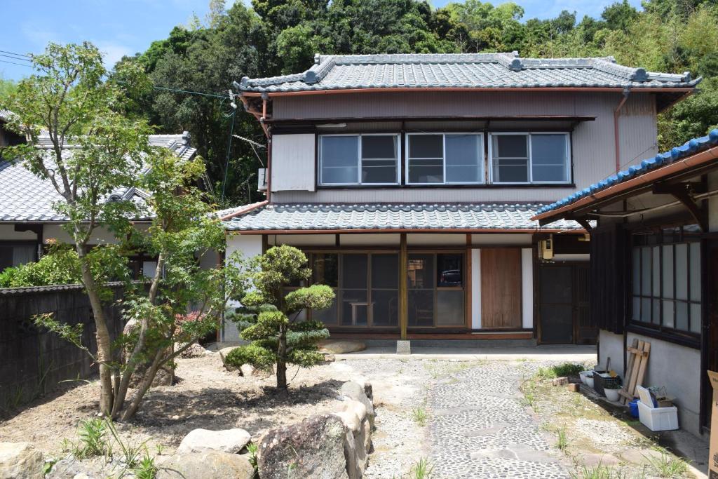 une maison japonaise avec une passerelle en pierre devant elle dans l'établissement ゲストハウス三軒家, à Shirahama
