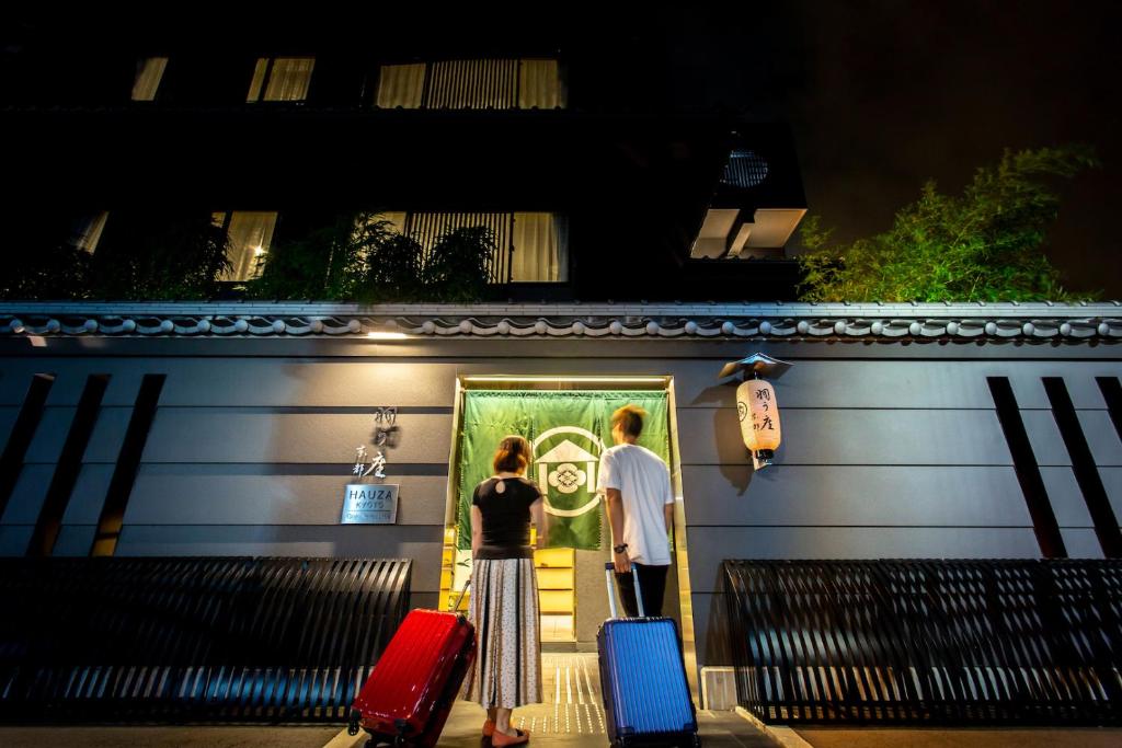 zwei Personen, die mit ihrem Gepäck vor einem Gebäude stehen in der Unterkunft HAUZA Kyoto Gojo Karasuma in Kyoto