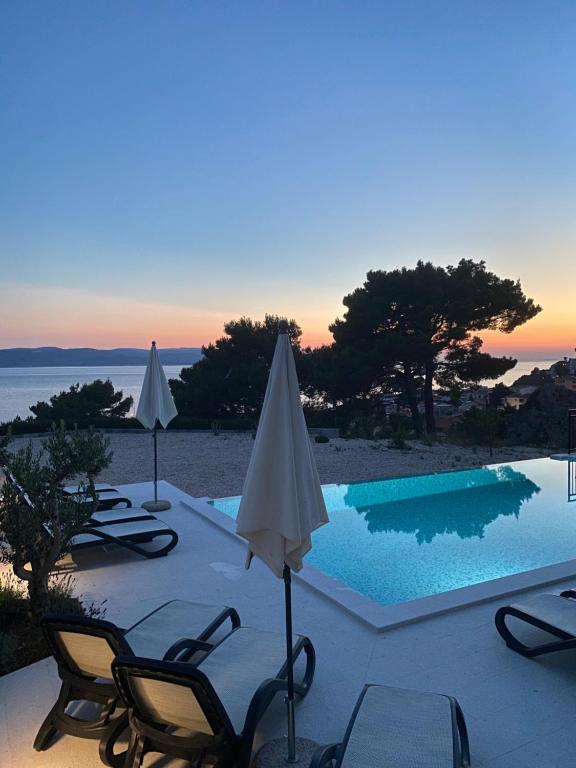 a pool with chairs and umbrellas next to the ocean at Baltimore.House in Baška Voda