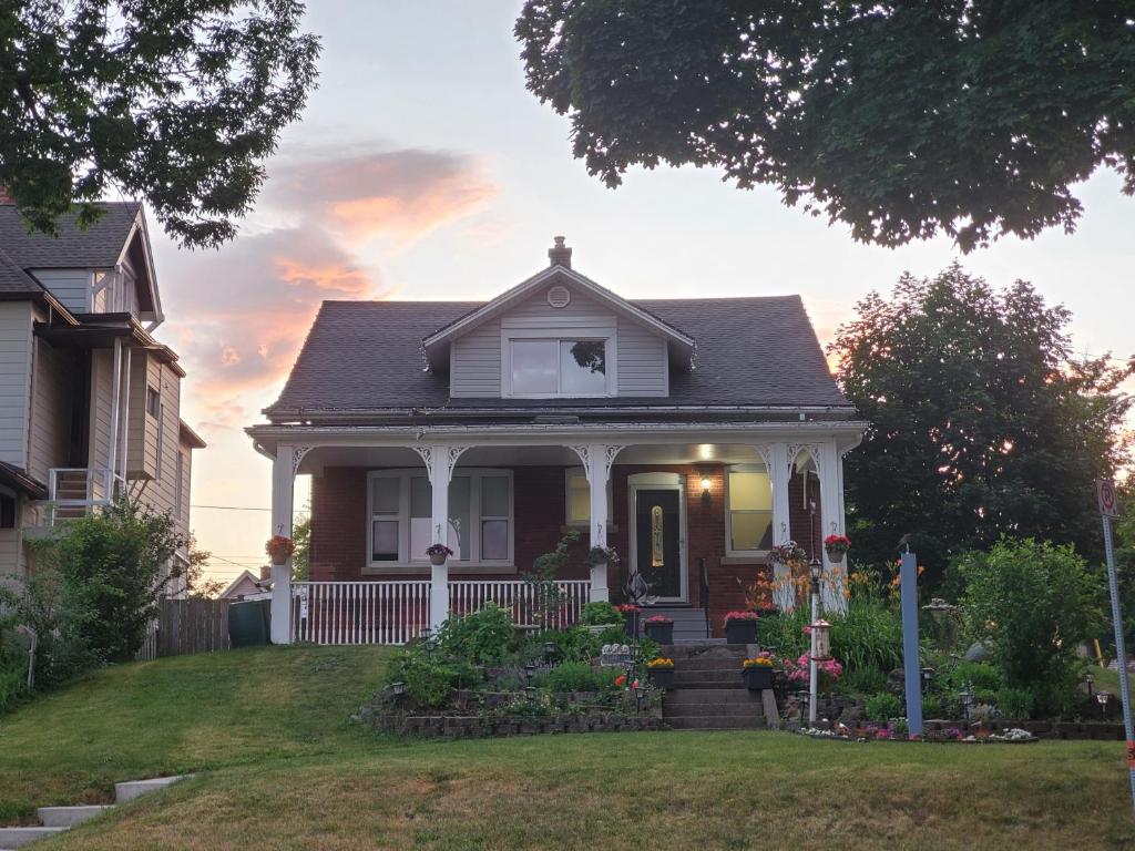 a white house with a porch with flowers in the yard at Serene Niagara Inn in Niagara Falls