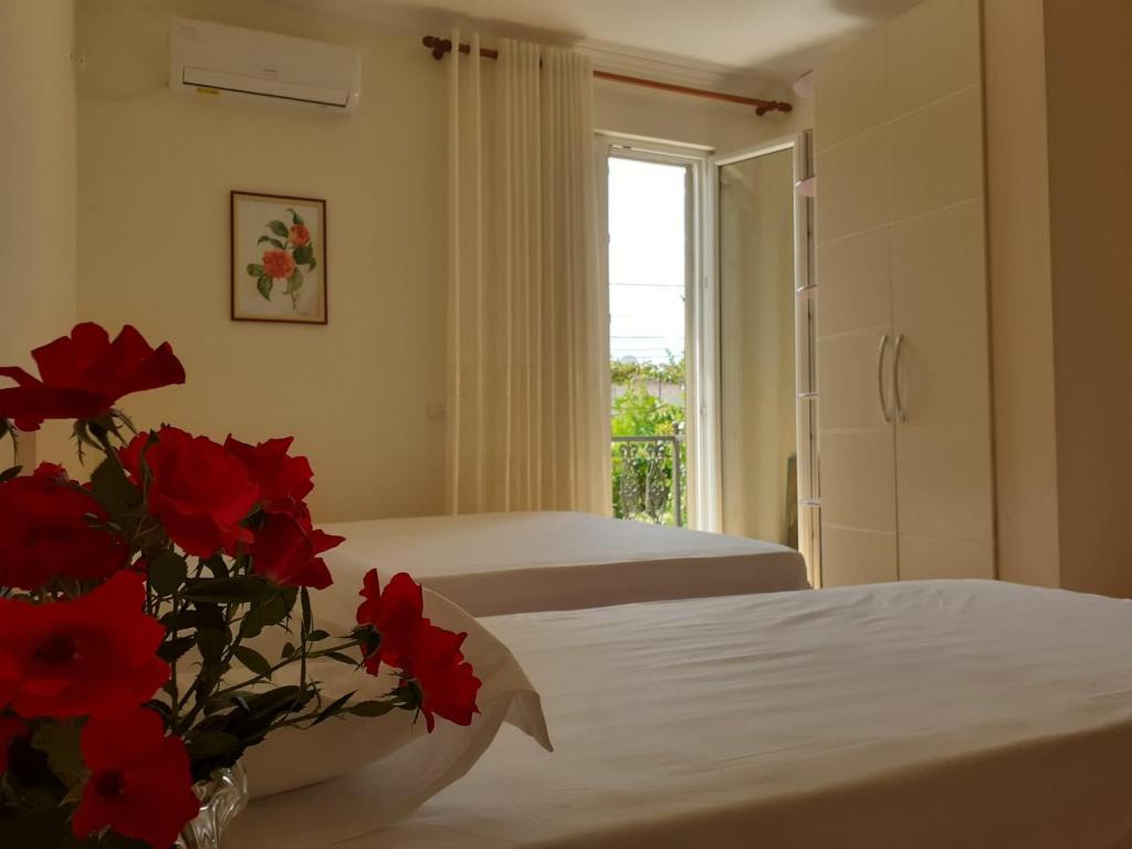 1 dormitorio con 2 camas y un jarrón de flores rojas en Guest House Zadeja, en Shkodër