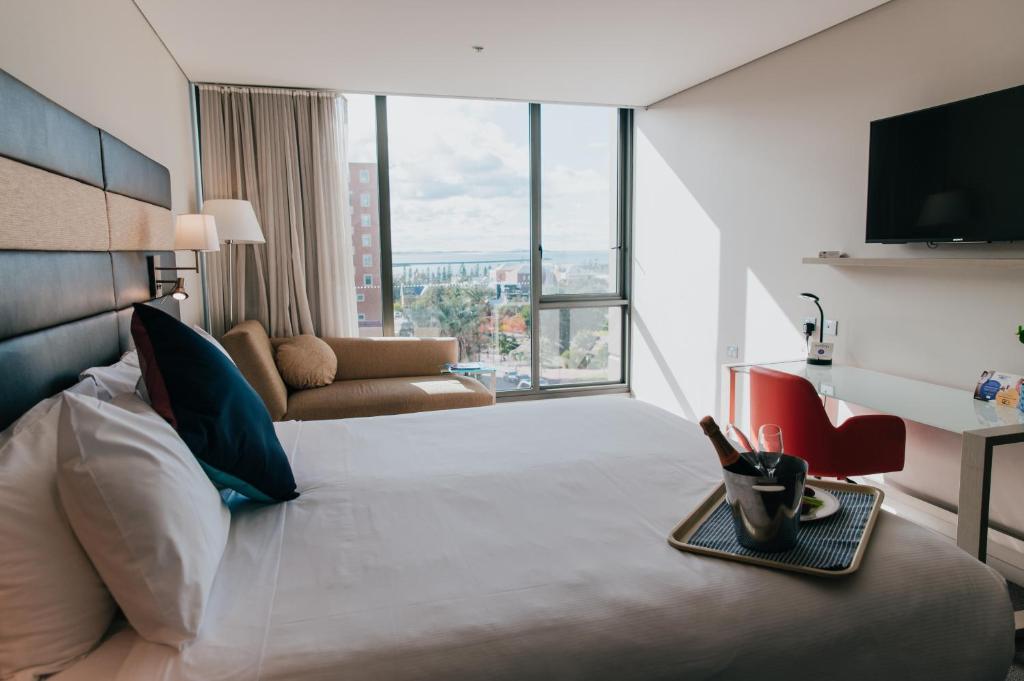 a hotel room with a large bed with a large window at Novotel Newcastle Beach in Newcastle