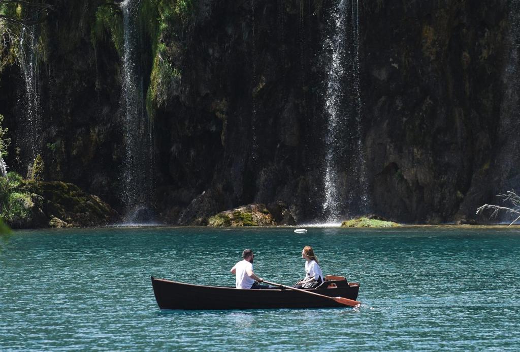 two people in a boat in the water near a waterfall at Guest House Lisina in Poljanak