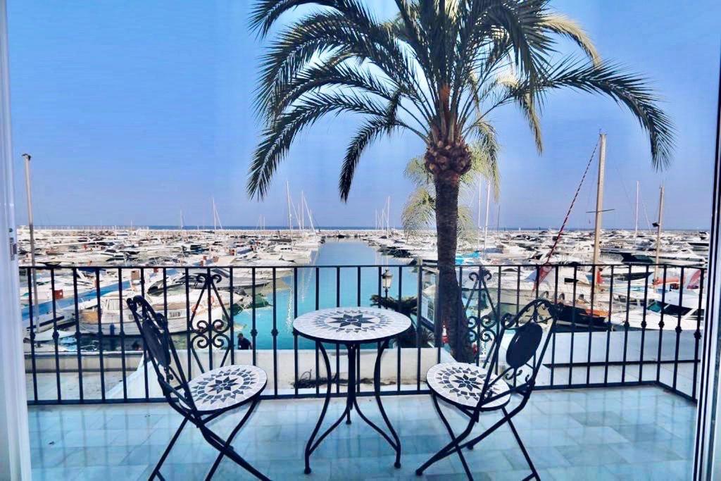 First Line Puerto Banus Harbour, 3 bedroom Luxury Apartment, Marbella في مربلة: بلكونة فيها نخلة وطاولة وكراسي