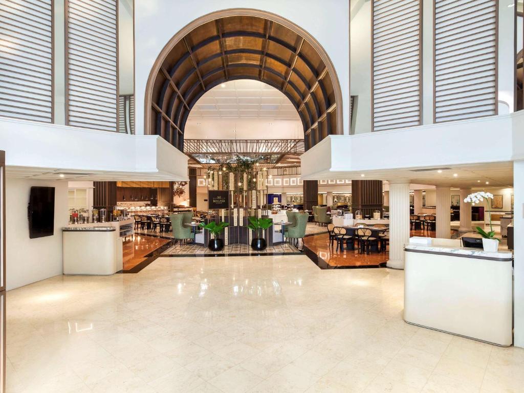 a lobby with a restaurant with tables and chairs at Mercure Jakarta Batavia in Jakarta