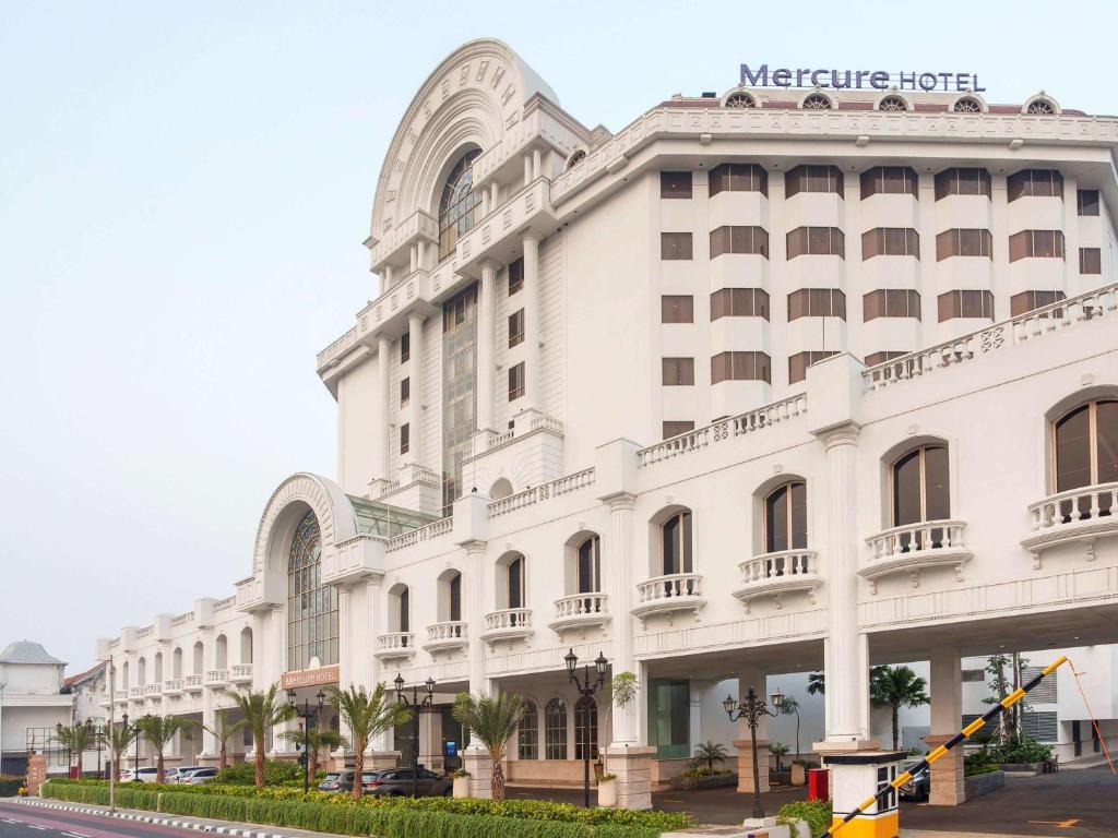 a large white building with palm trees in front of it at Mercure Jakarta Batavia in Jakarta