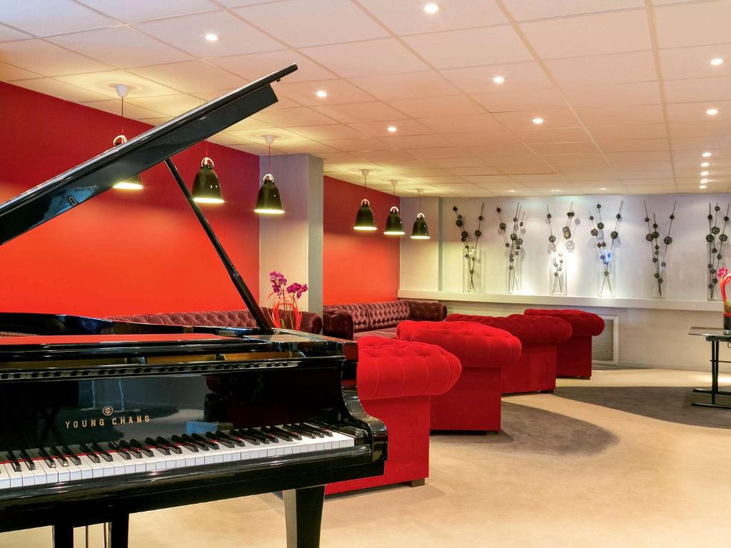 a living room with a piano and red chairs at Mercure Bordeaux Lac in Bordeaux