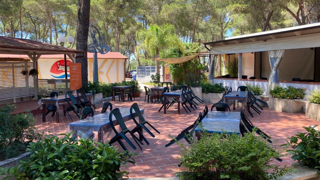 un patio con mesas, sillas, mesas y árboles en Riva dei Greci Camping Village, en Metaponto