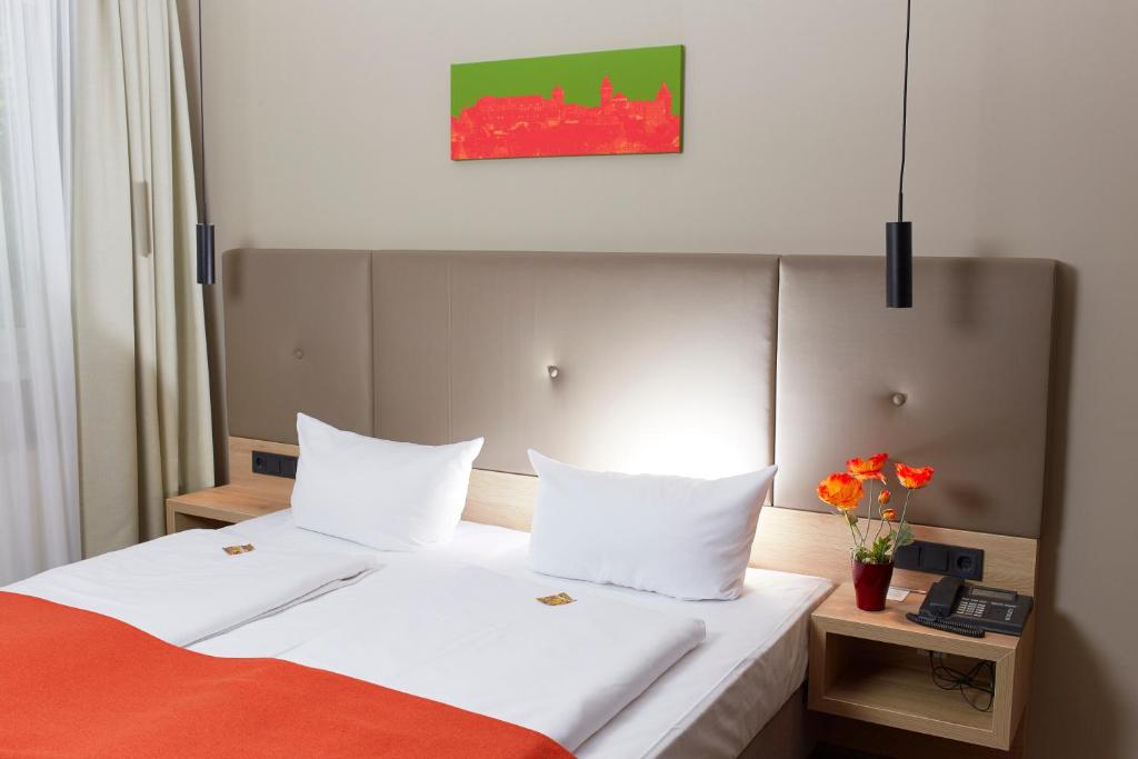 ein Hotelzimmer mit einem Bett mit weißer Bettwäsche und orangefarbener Decke in der Unterkunft Hotel Alpha in Nürnberg