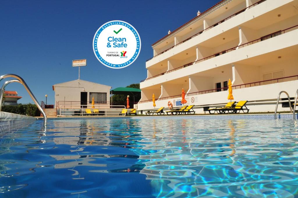 a swimming pool in front of a hotel with the clean safe logo at Solgarve in Quarteira