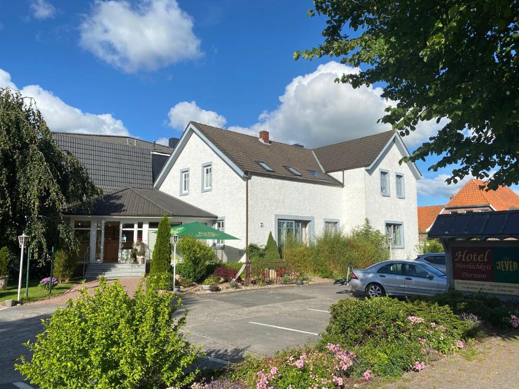 a white house with a car parked in a parking lot at Hotel Herrlichkeit Dornum Janßen in Dornum