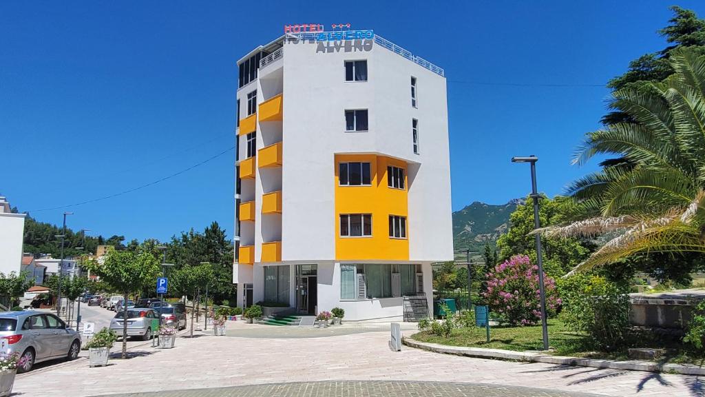 un bâtiment blanc et jaune avec un parking dans l'établissement Alvero Hotel, à Përmet