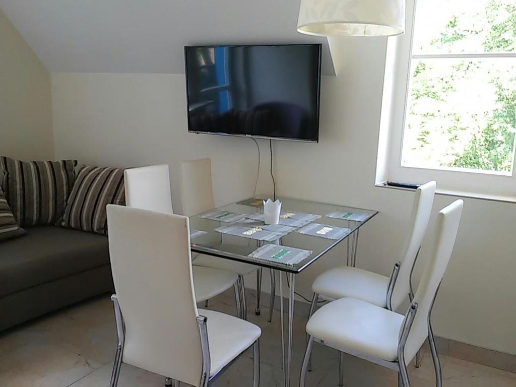 a dining room table with chairs and a television on the wall at Pergolt Apartment in Pervalka