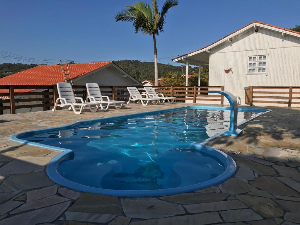 a swimming pool with chairs and a palm tree at Pousada Essência do Rosa in Praia do Rosa