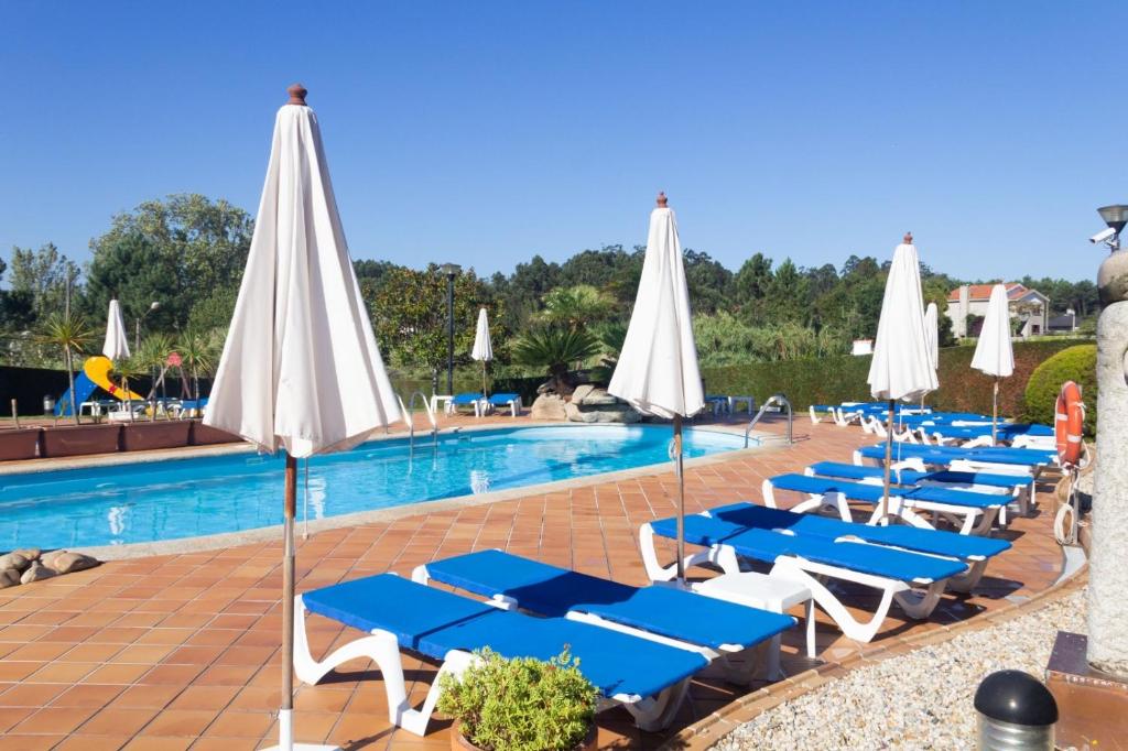 una piscina con sedie a sdraio e ombrelloni blu e bianchi di Hotel Canelas a Portonovo