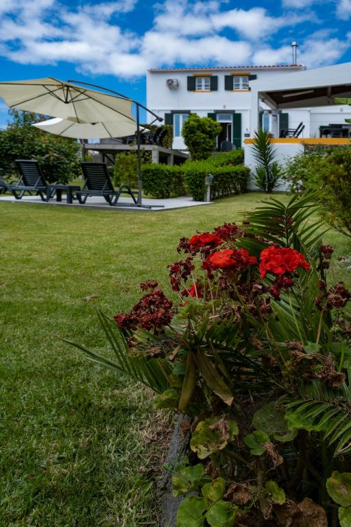 a house with a garden with red flowers and an umbrella at Casa da Quinta in Vila Franca do Campo