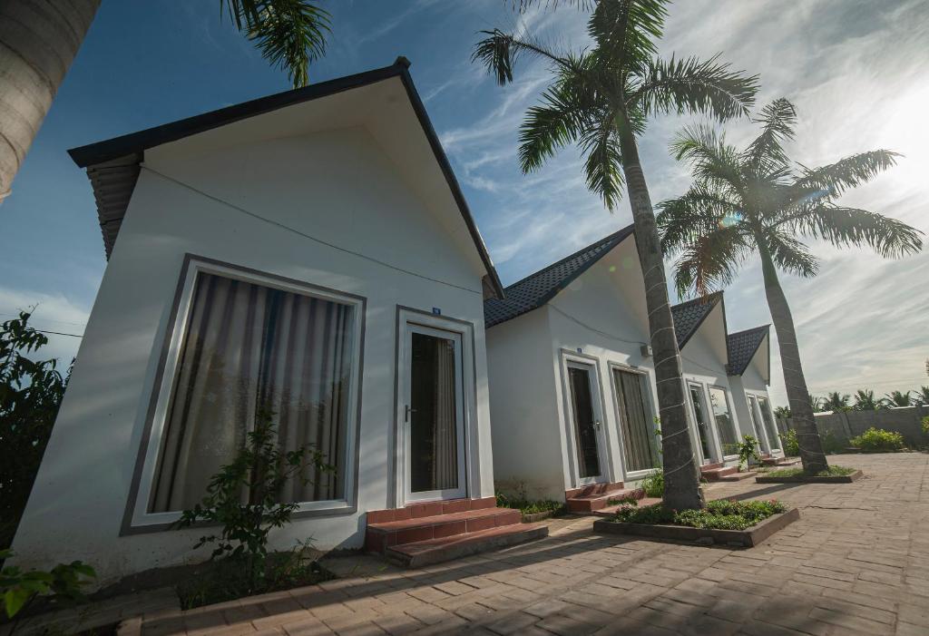 a white house with palm trees in front of it at FaMi Nguyễn Homestay Châu Đốc in Chau Doc