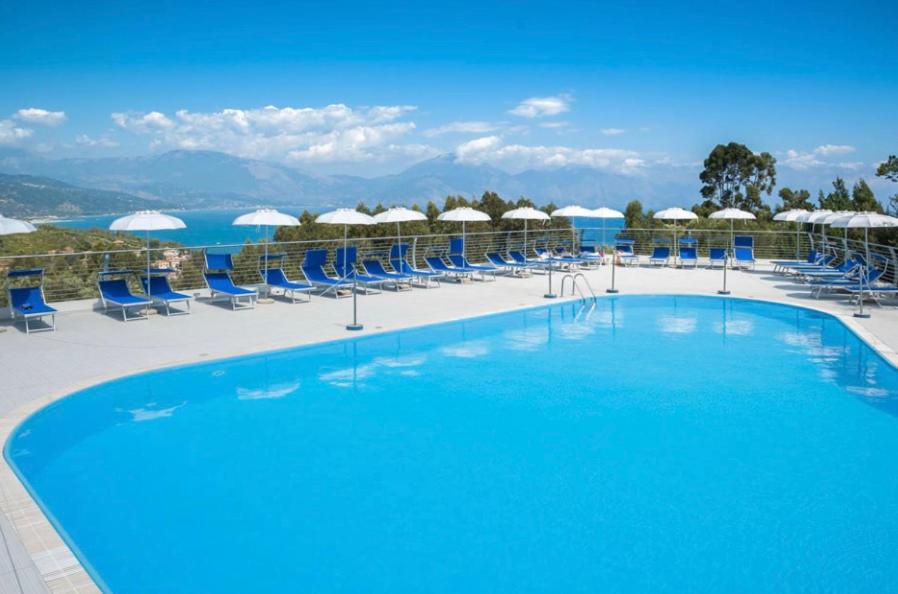 a large swimming pool with blue chairs and umbrellas at Marcaneto Hotel in Scario