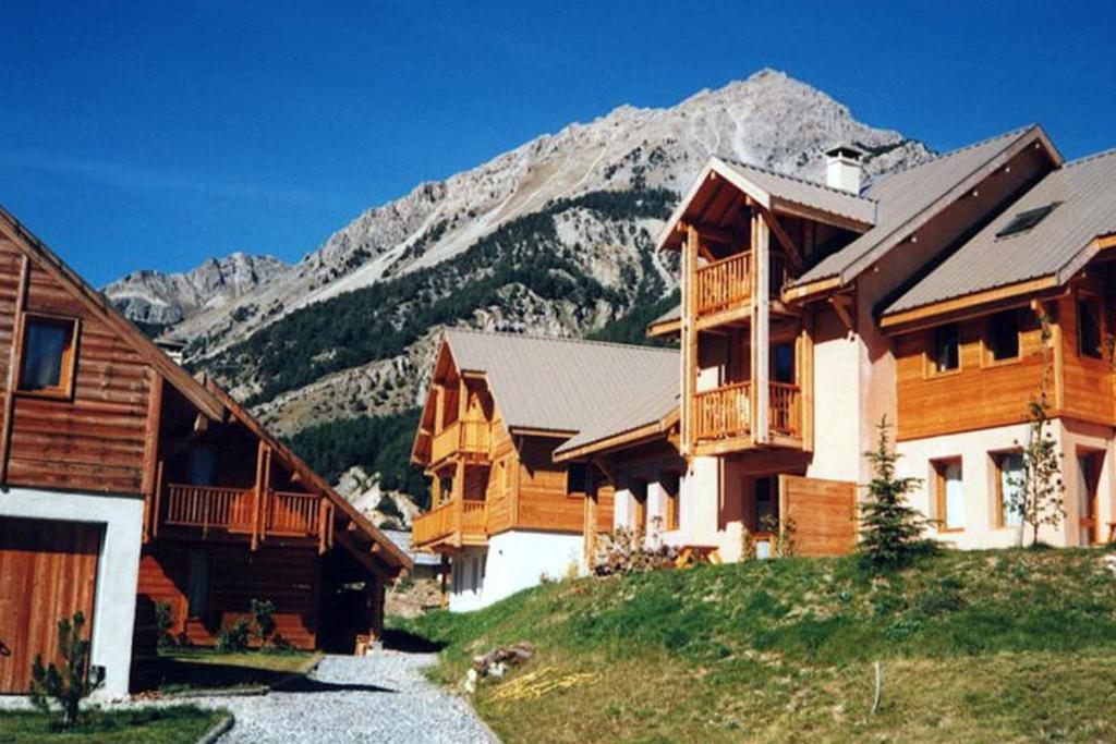 un grupo de edificios de madera con una montaña en el fondo en Le Barlèt23 pers Hameau des Chazals Nevache Hautes Alpes, en Névache