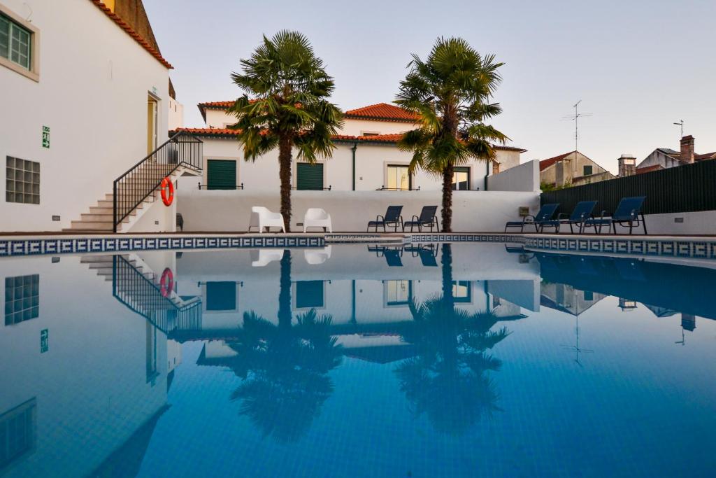a swimming pool with chairs and palm trees next to a building at O Paço - exclusive accommodation in Tomar