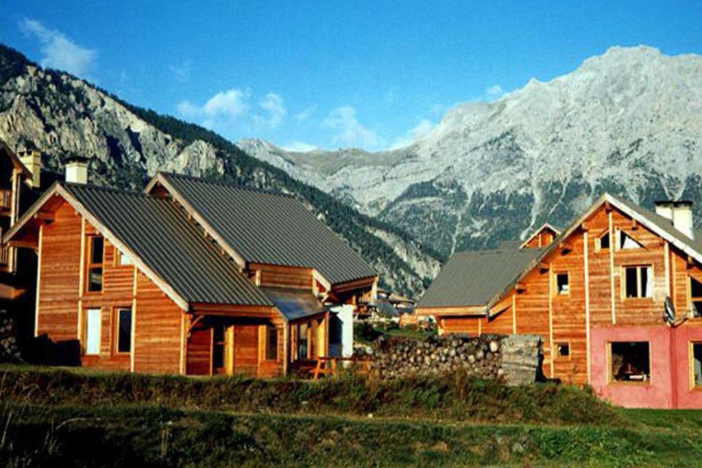 a wooden house with mountains in the background at Le Baoùba Hameau des Chazals Nevache Hautes Alpes in Névache