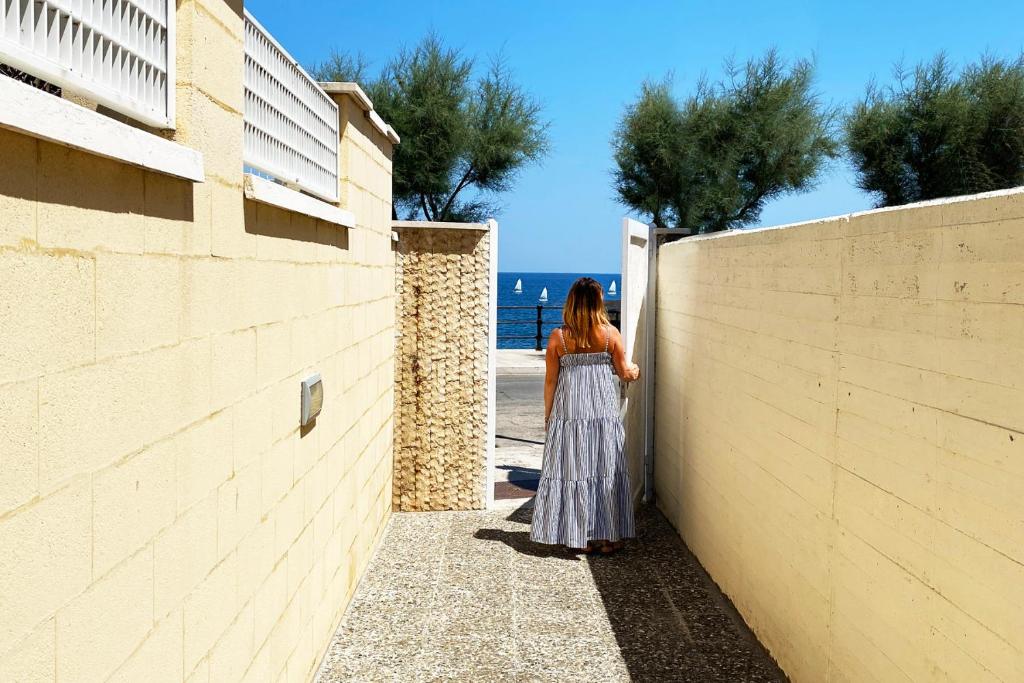 a woman standing next to a wall looking at the ocean at La Rotonda - Casa vacanze in Giovinazzo
