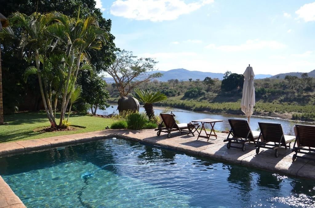 a swimming pool with chairs and a table and an umbrella at Khandizwe Kruger Villa in Malelane