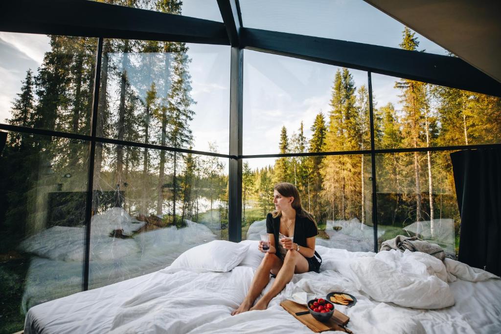 una mujer sentada en una cama en una habitación con ventanas en Magical Pond Nature Igloos, en Ruka