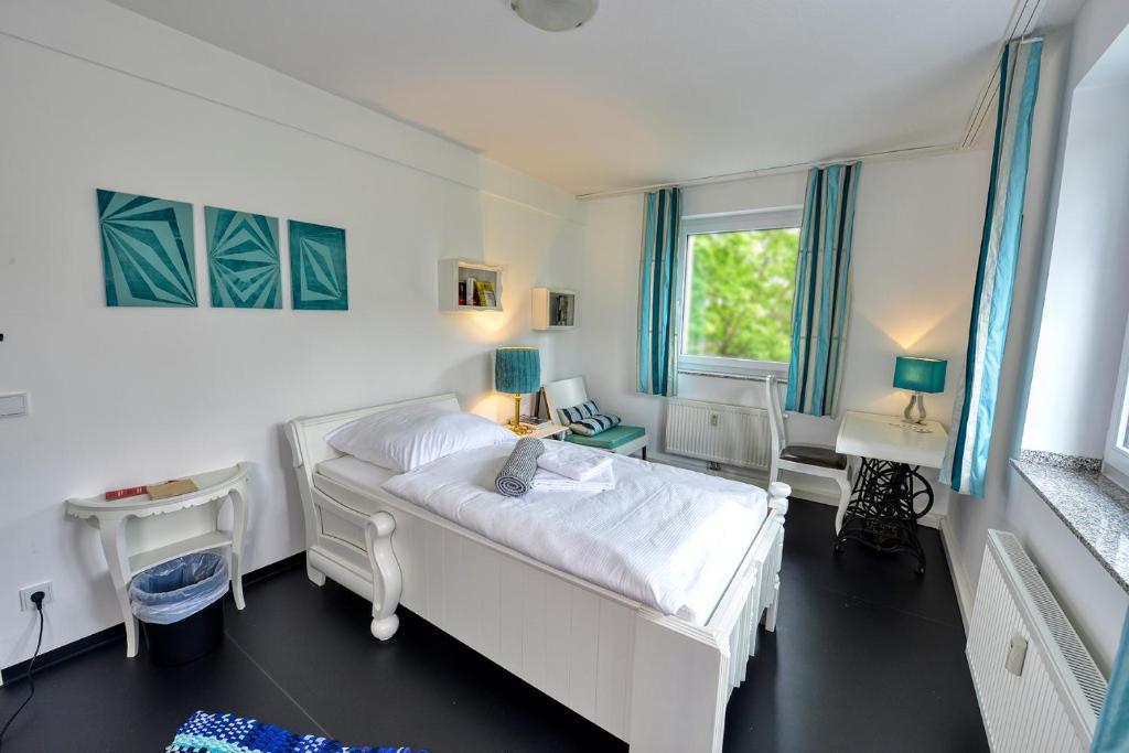 a bedroom with a white bed and a desk at Hostel am Niederfeldsee in Essen