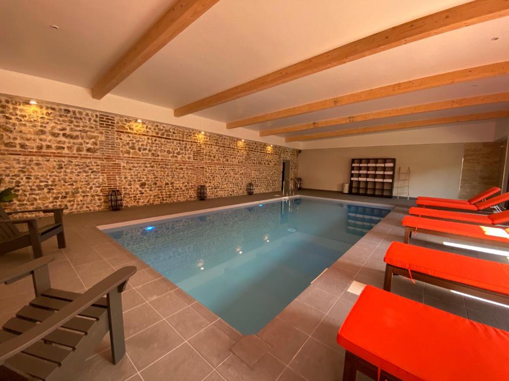 une grande piscine avec des tables rouges et des chaises dans l'établissement Hôtel-Spa-Piscine Le Petit Castel Beuzeville-Honfleur, à Beuzeville