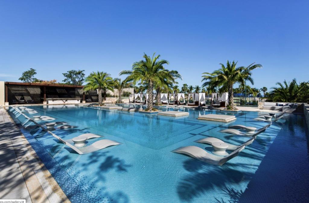 a large swimming pool with lounge chairs and palm trees at Bohari Palmilla in San José del Cabo