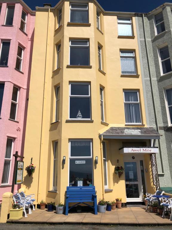 a yellow building with a blue bench in front of it at Awel Mor in Criccieth