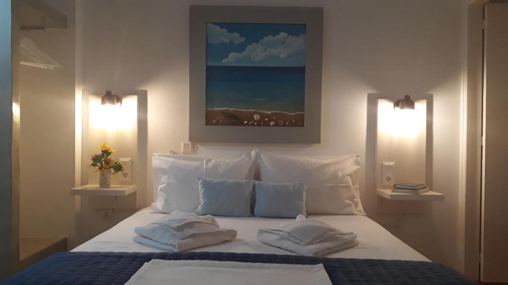 a bedroom with a bed with white pillows and a painting at Katerina Rooms in Tinos