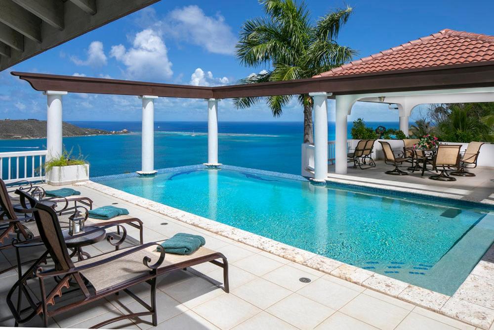 a swimming pool with chairs and the ocean in the background at TAMAR VILLA in Virgin Gorda