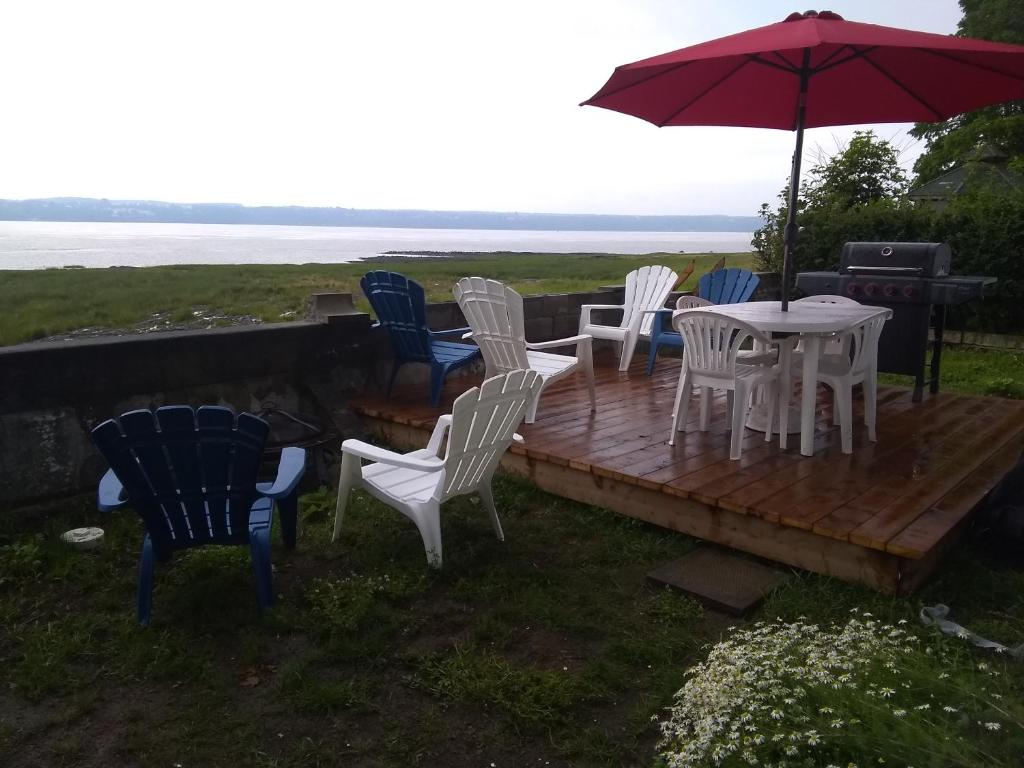 a wooden deck with chairs and a table with an umbrella at La Maison Vaillancourt in Saint-Laurent-de-l'ile d'Orleans