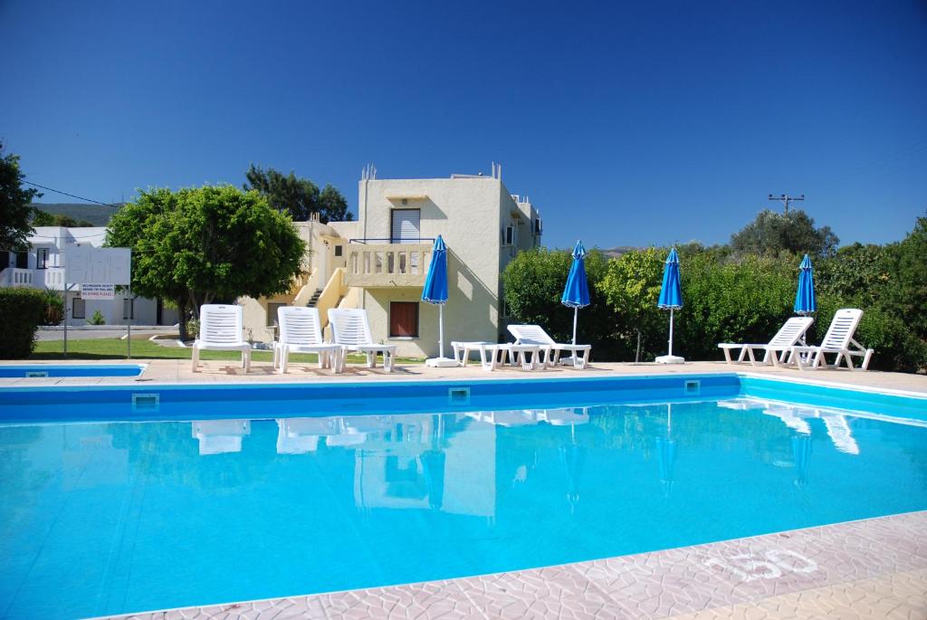 a swimming pool with chairs and blue umbrellas at Angelos Studios in Kos