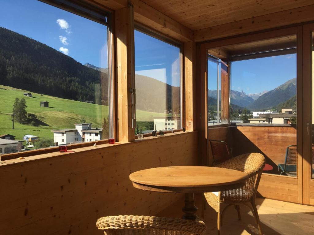 une table et des chaises dans une chambre avec une grande fenêtre dans l'établissement Vinadi, à Davos