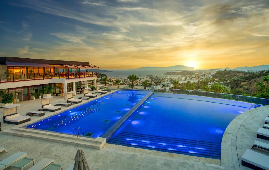 a hotel with a large swimming pool with chairs and the sunset at Hillstone Bodrum Hotel & Spa in Bodrum City