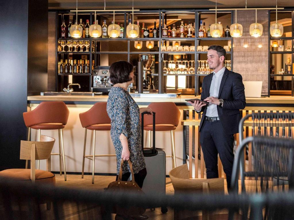 Ein Mann und eine Frau stehen vor einer Bar in der Unterkunft Mercure Luxembourg Off Kirchberg in Luxemburg (Stadt)