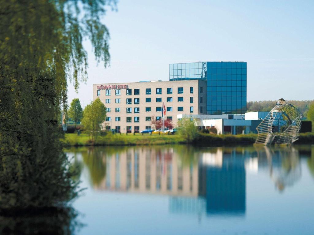 a man standing next to a body of water with a building at Mövenpick Hotel 's Hertogenbosch in Den Bosch